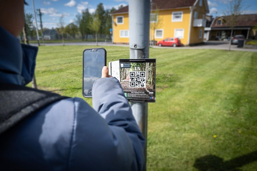 Pojke scannar QR-kod för X-rundan på en lyktstolp med sin telefon.