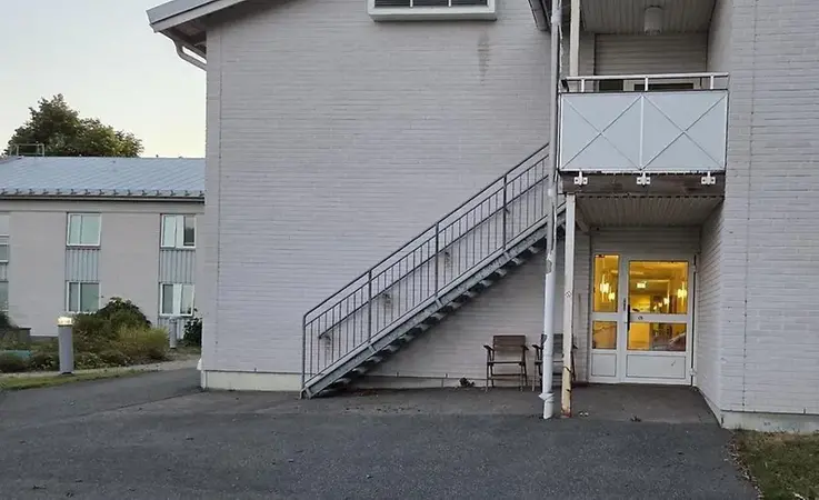 Vit tegelbyggnad i skymning, upplyst ingång på gavel.