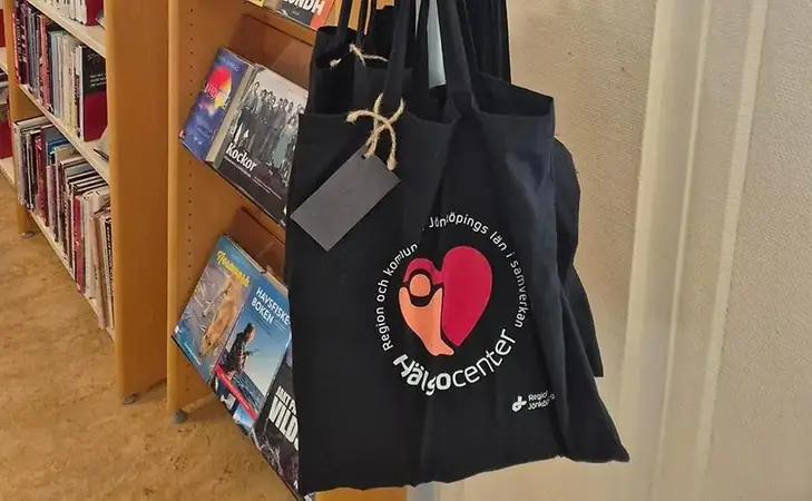 Svart tygpåse med logga Hälsocenter hänger i ett bibliotek.